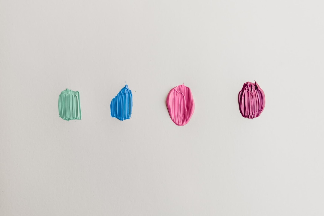 Photograph of four small paint samples, in green, blue, pink, and magenta, against a flat off white background