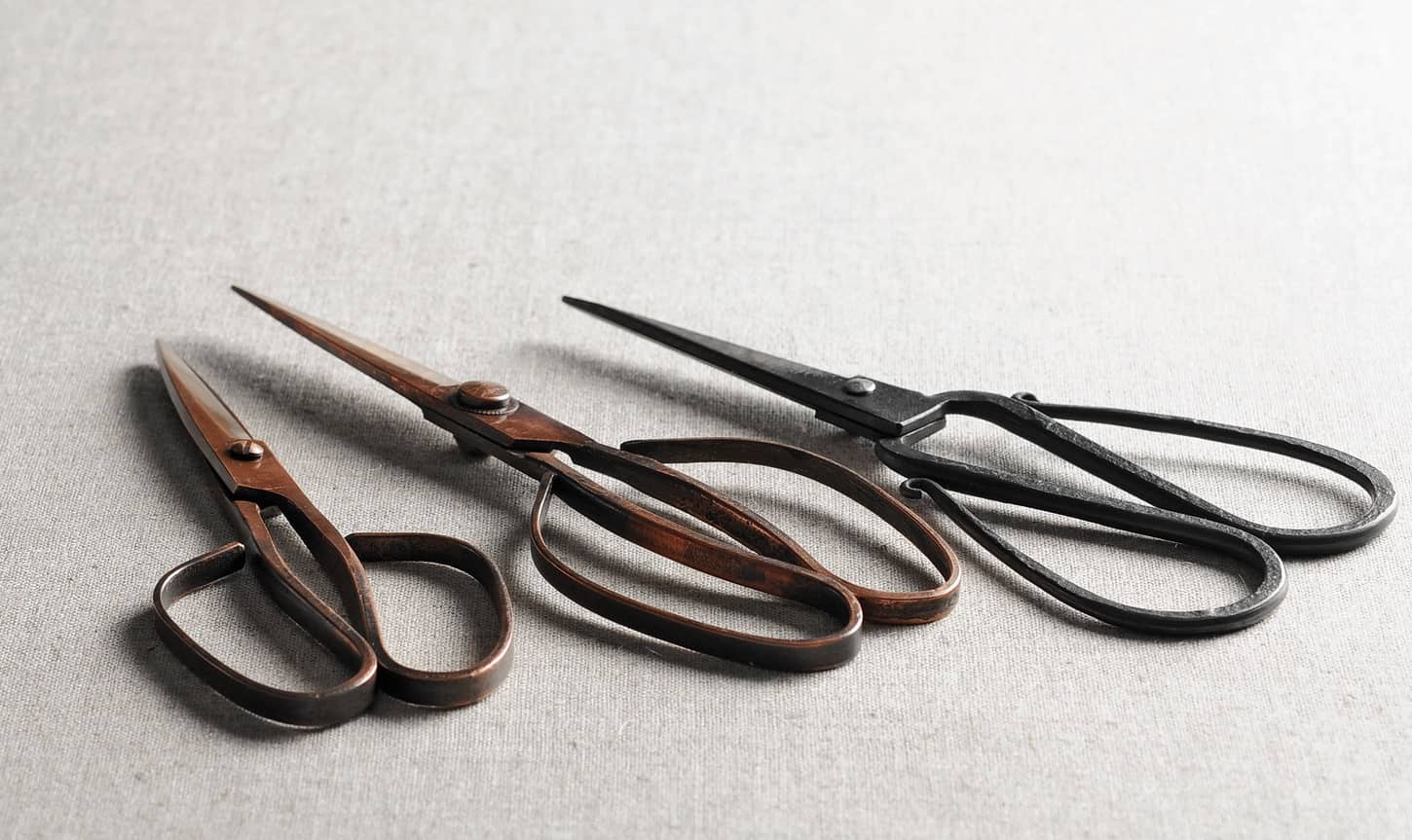 Three pairs of rustic looking Japanese scissors laying on a piece of light grey cloth