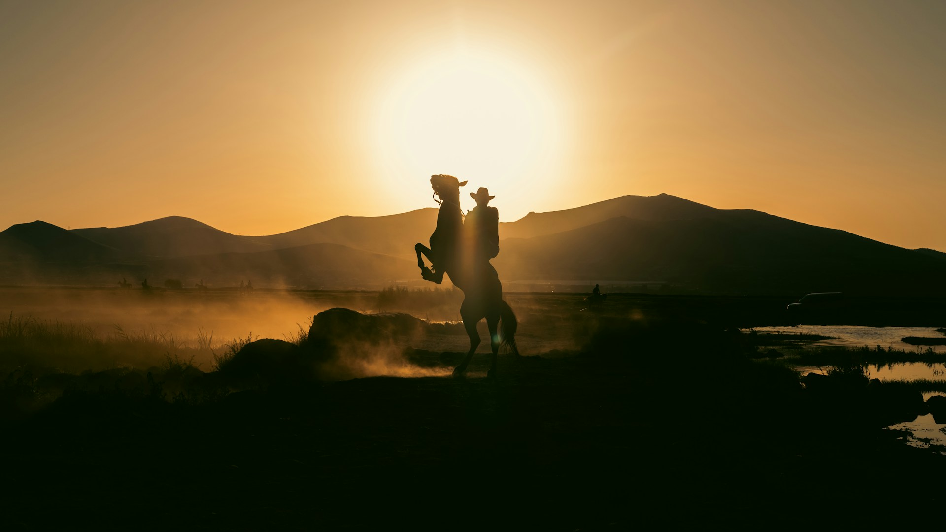 A cowboy on a rearing horse at sunset in a desert valley