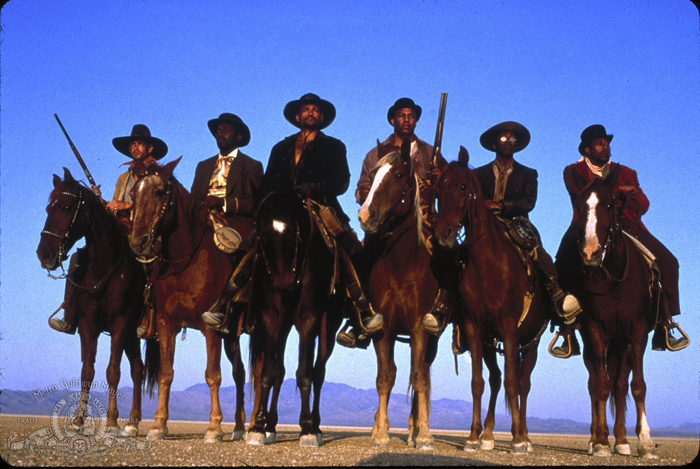 Six cowboys on horseback, with the mountains behind them.